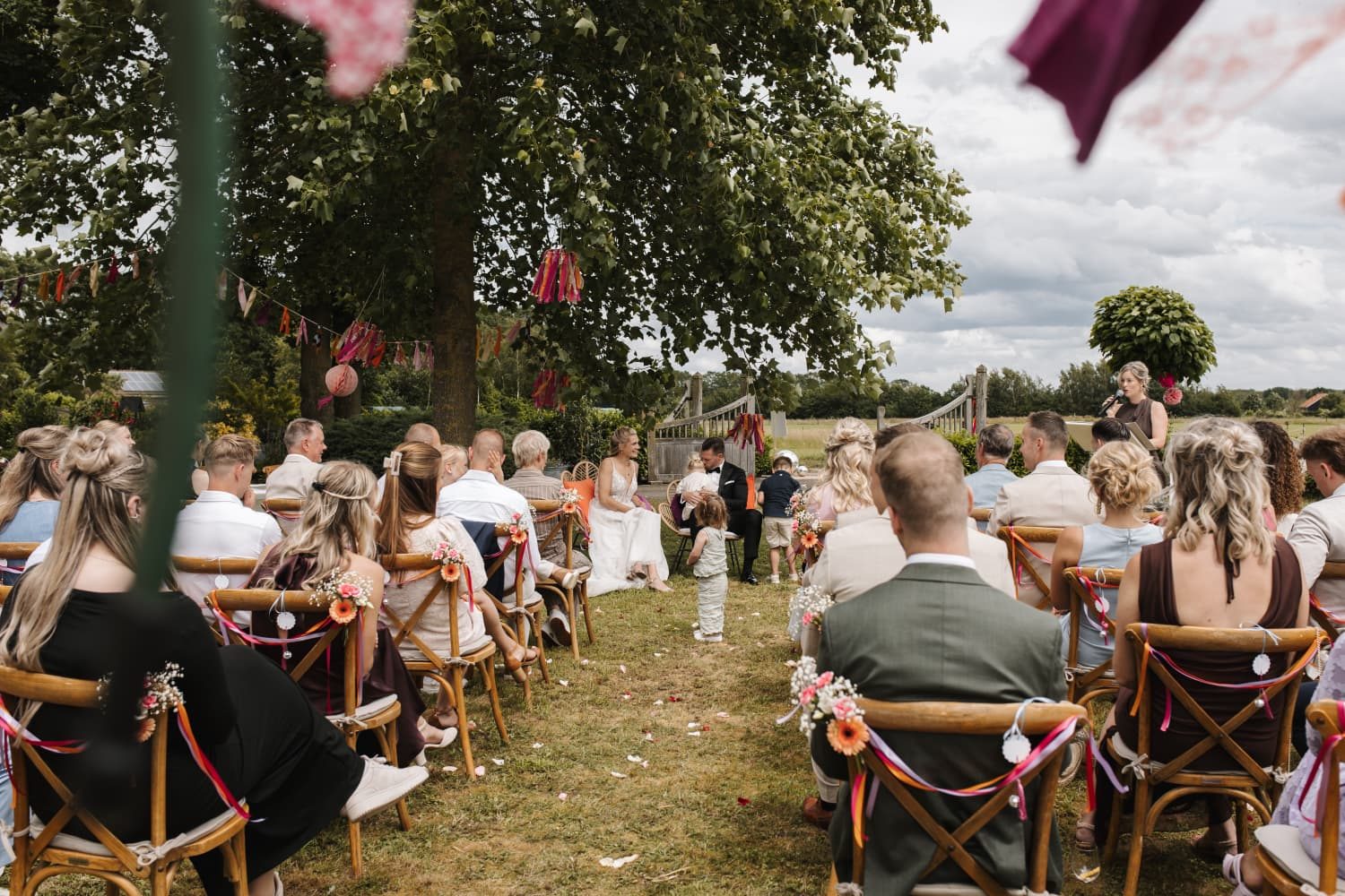 Gasten kijken naar het bruidspaar tijdens een ceremonie in de tuin
