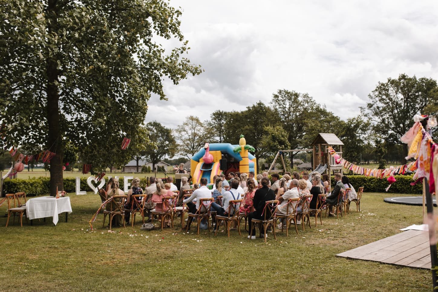 Ceremonie in de buitenlucht met gasten op houten stoelen